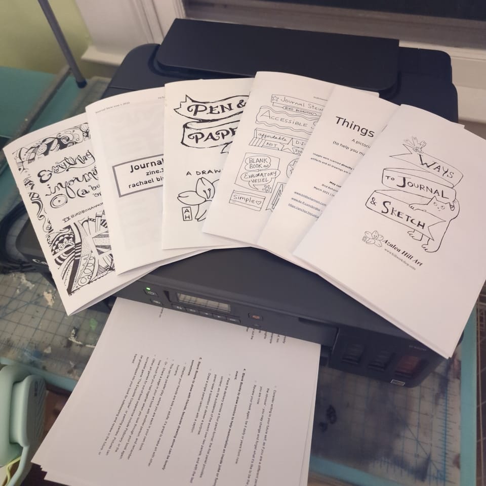 Zines fanned out on printer while printer continues to print more copies